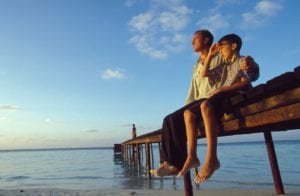 Father puts his arm around son while sitting on a dock