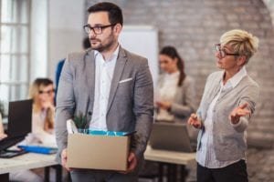 Fired employee holds a box of his items as a woman points him to the door