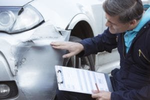 Man with clipboard examines damaged car in no fault accident