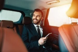 Businessman with phone on hand sitting on the backseat of the car