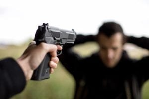 Man pointing a gun to another man with hands on his head