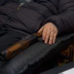 A man sitting with a shotgunn in armchair, concept of home self defense