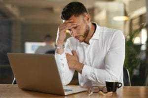 Man looking at his laptop in worry while holding his head in his hand