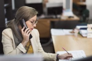 Woman writing on the table and using the telephone