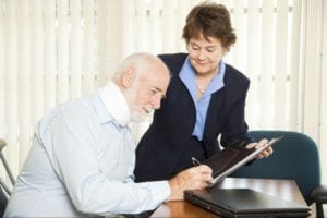 Woman assisting an injured elderly man as he signs a piece of paper