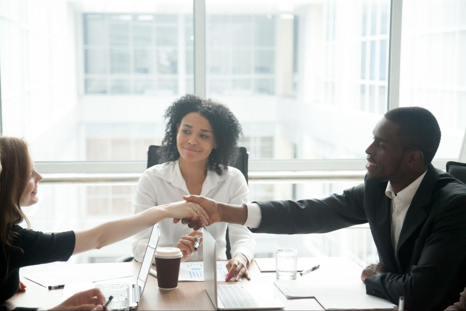 Woman smiling while her two colleagues shake hands