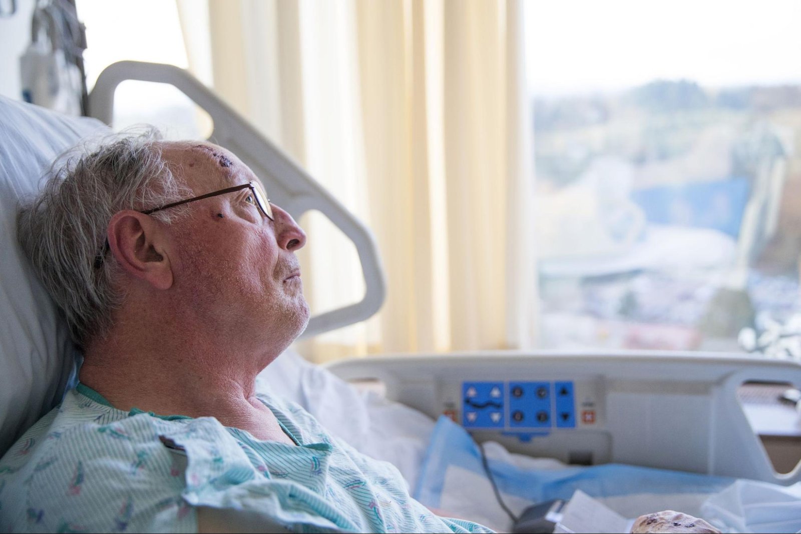 Elderly man looking out the window while lying in a hospital bed