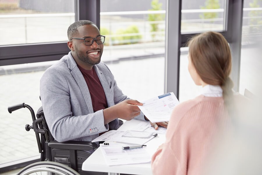 Smiling man in a wheelchair talking to a woman while holding a piece of paper