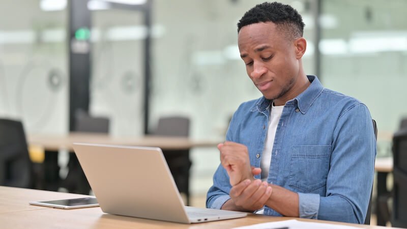 Man in front of his laptop and holding his aching wrist