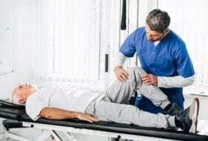 Male therapist training an elderly man with a fractured leg while lying down